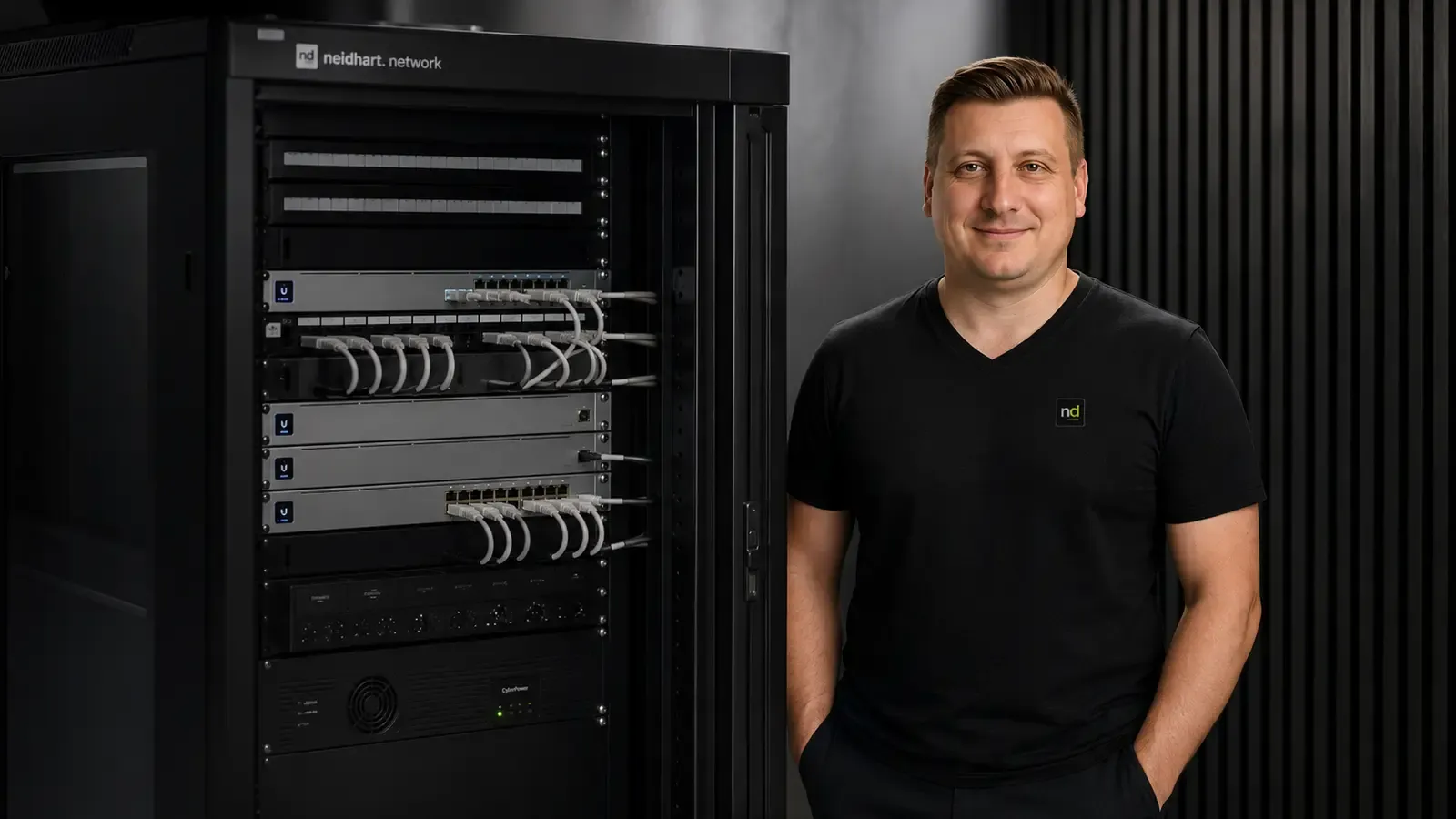 Christian Neidhart vor einem modernen UniFi-Netzwerkschrank